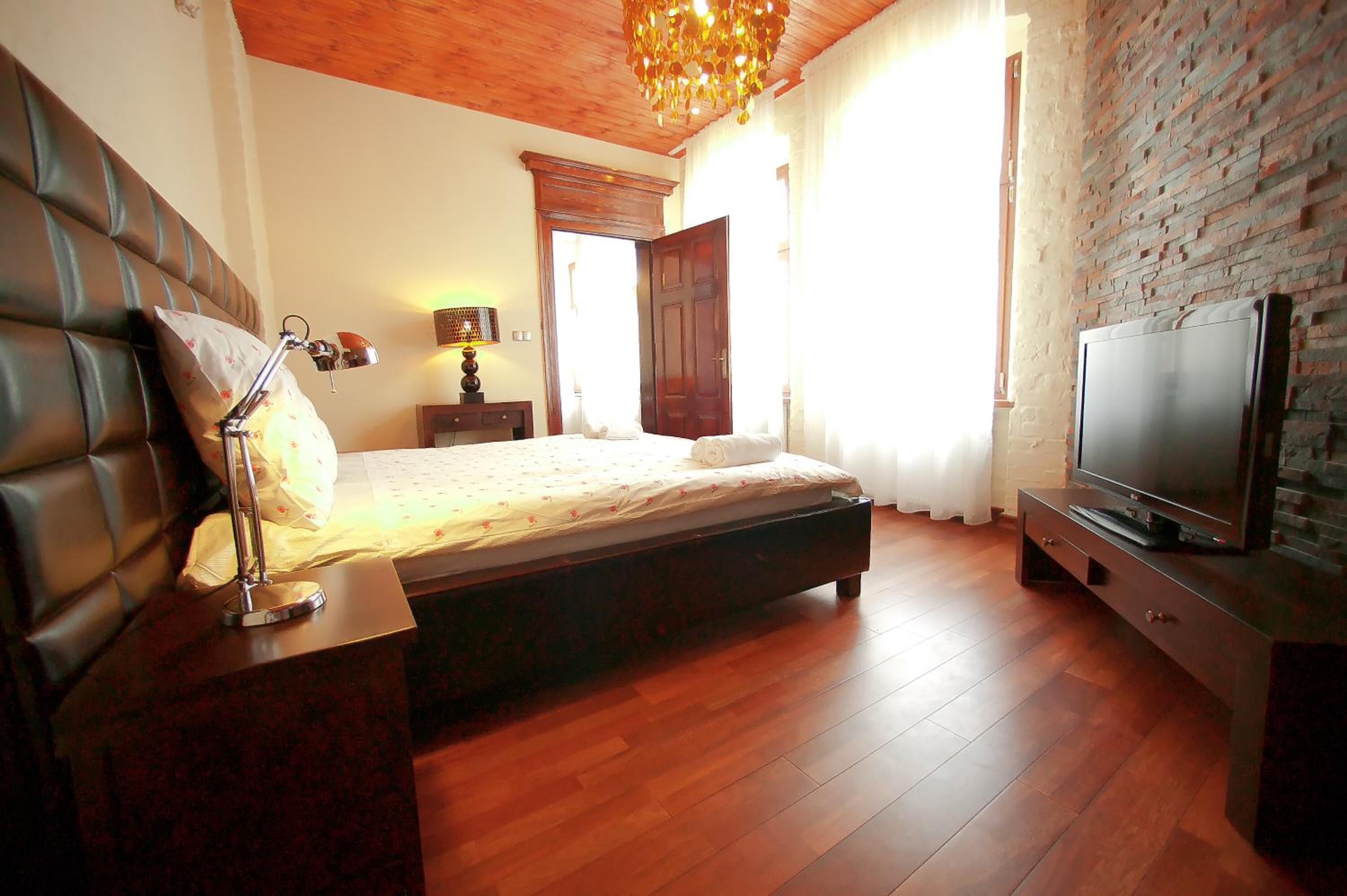Un dormitorio con cama, lámpara de noche, suelo de madera, pared de ladrillo y televisión sobre un mueble.