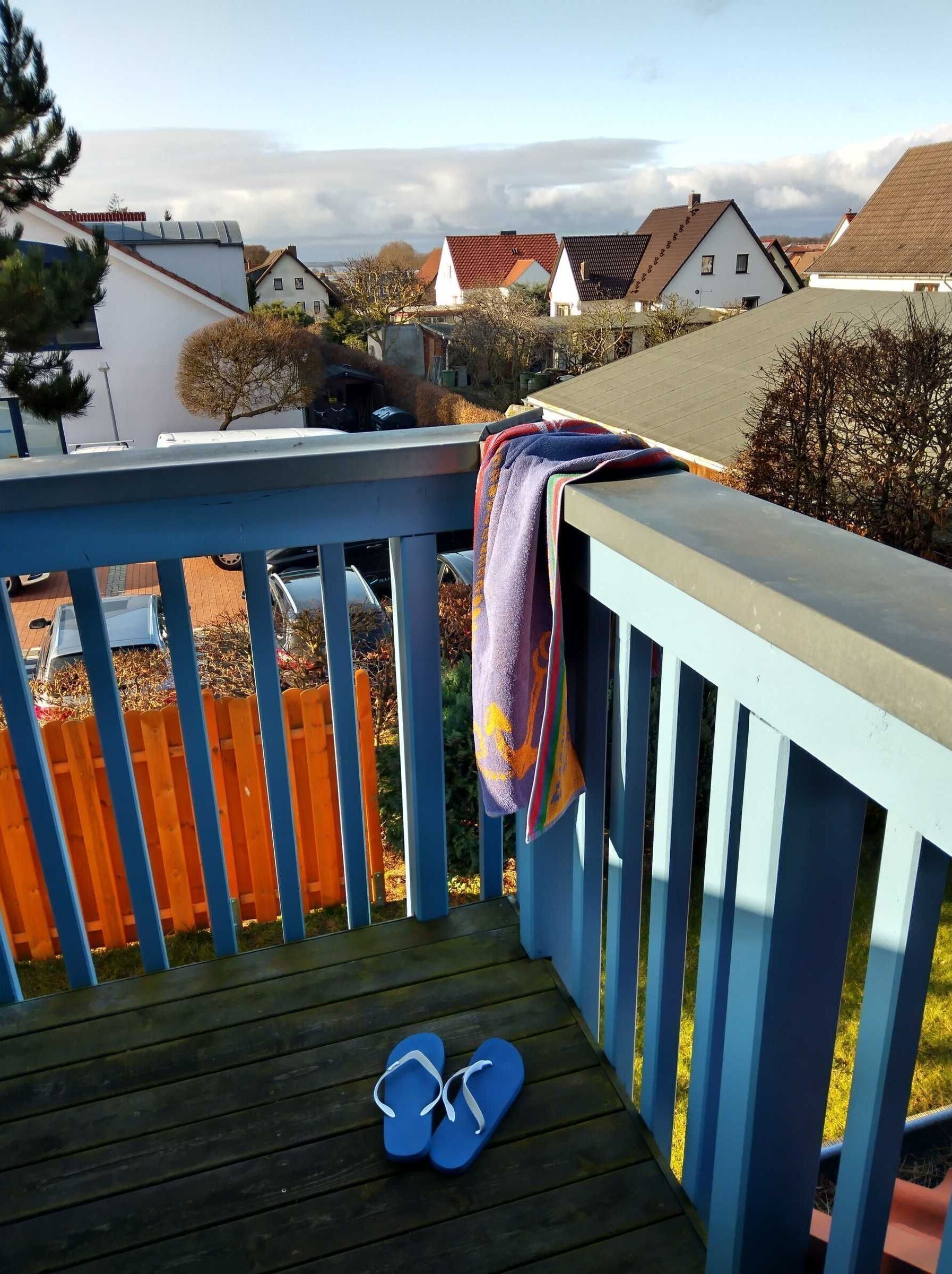 A wooden deck with a pair of blue flip-flops and a colorful towel hanging on the railing.