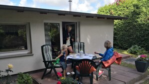 Un patio al aire libre con una mesa y sillas, rodeado de macetas con plantas y un jardín.