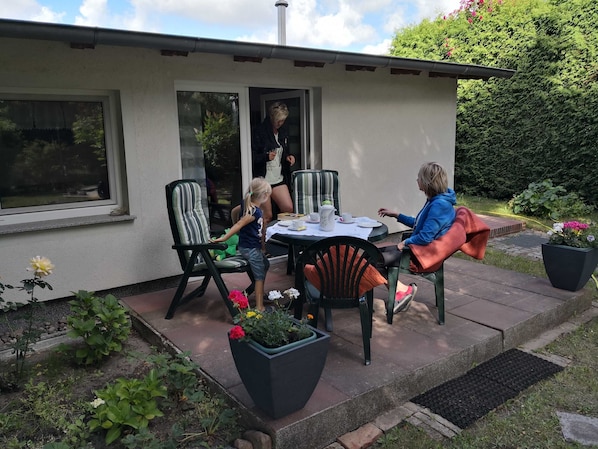 Une terrasse extérieure avec une table et des chaises, entourée de plantes en pot et d’un jardin.