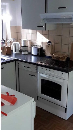 Une cuisine avec des meubles blancs, une cuisinière, un grille-pain et une machine à café.