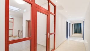 A modern hallway with red-framed glass doors, a staircase, and a view into another room.