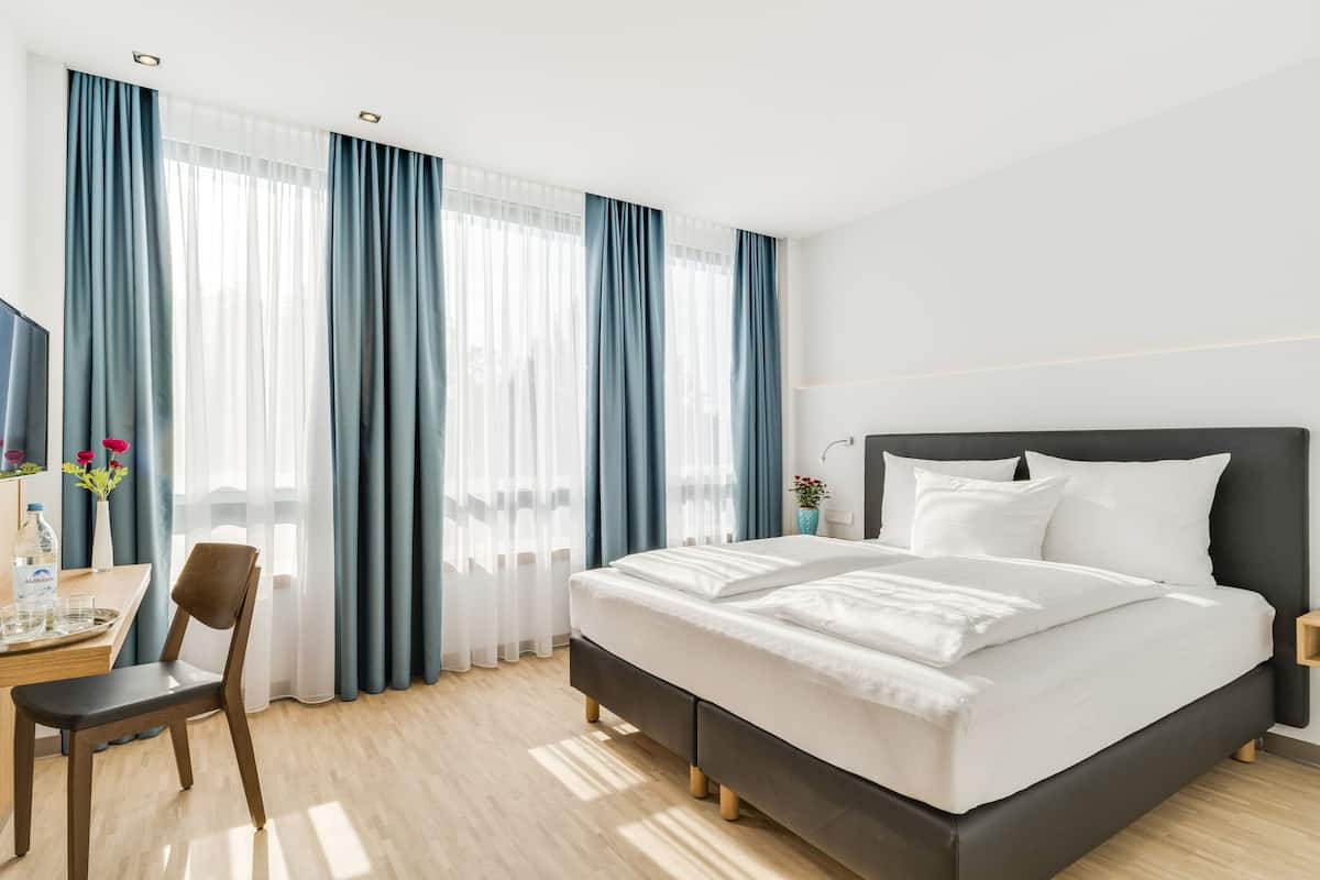 A hotel room with a bed, a desk, and a chair.