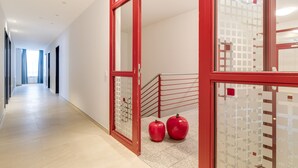 A hallway with a red-framed door, a staircase, and two red apples on the floor.
