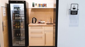 A kitchenette with a refrigerator stocked with beverages, a coffee maker, and a tea kettle.