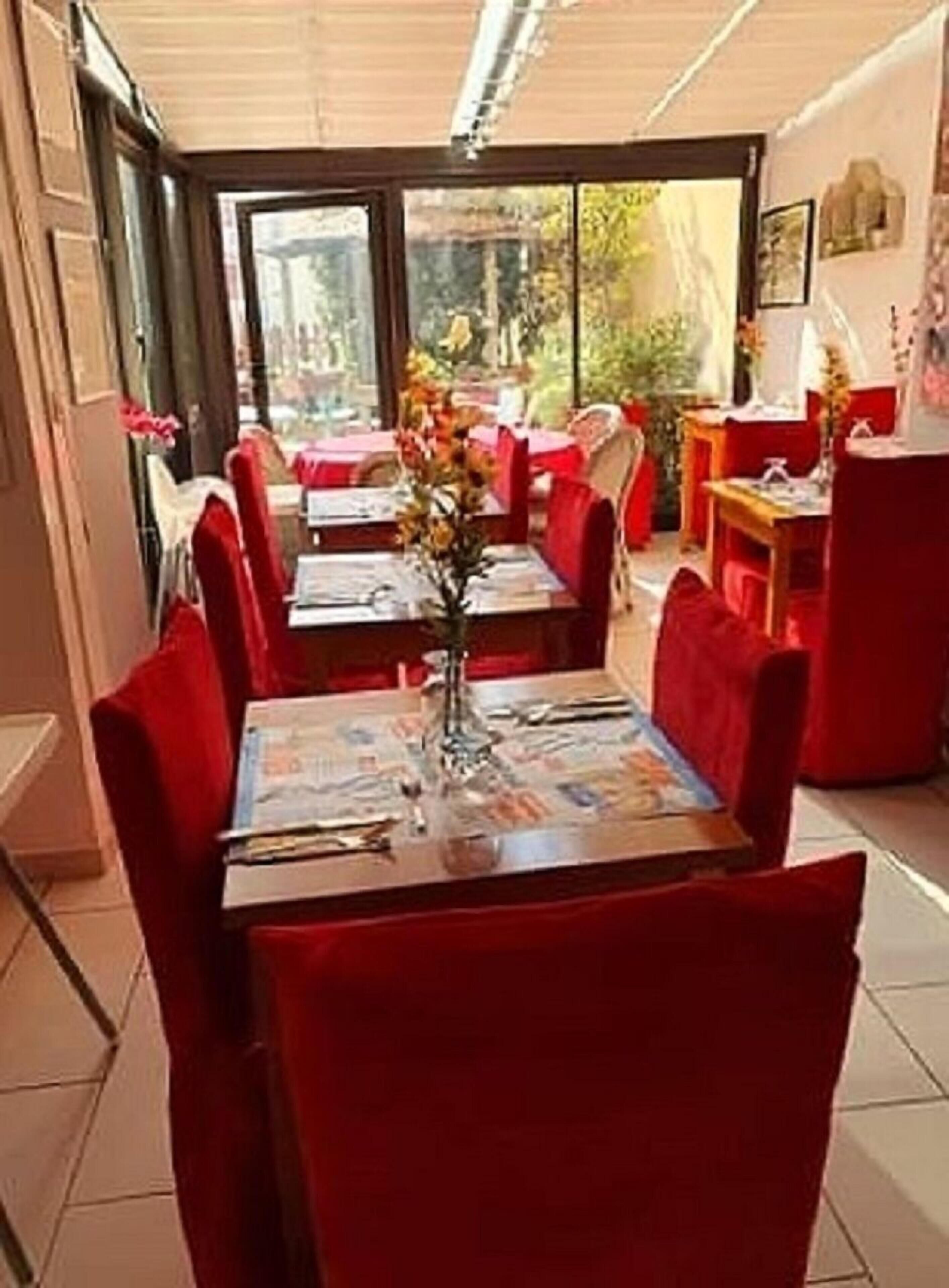 En restaurang med röda stolar och bord, en vas med blommor och utsikt över grönområden utanför.