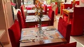 En restaurang med röda stolar och bord, en vas med blommor och utsikt över grönområden utanför.