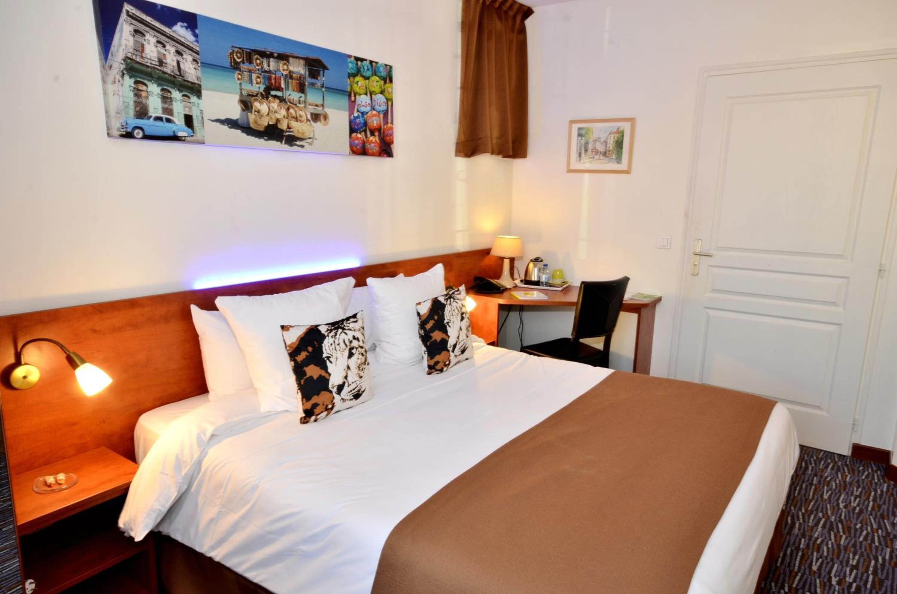 A hotel room with a large bed, a desk, a chair, and a door.