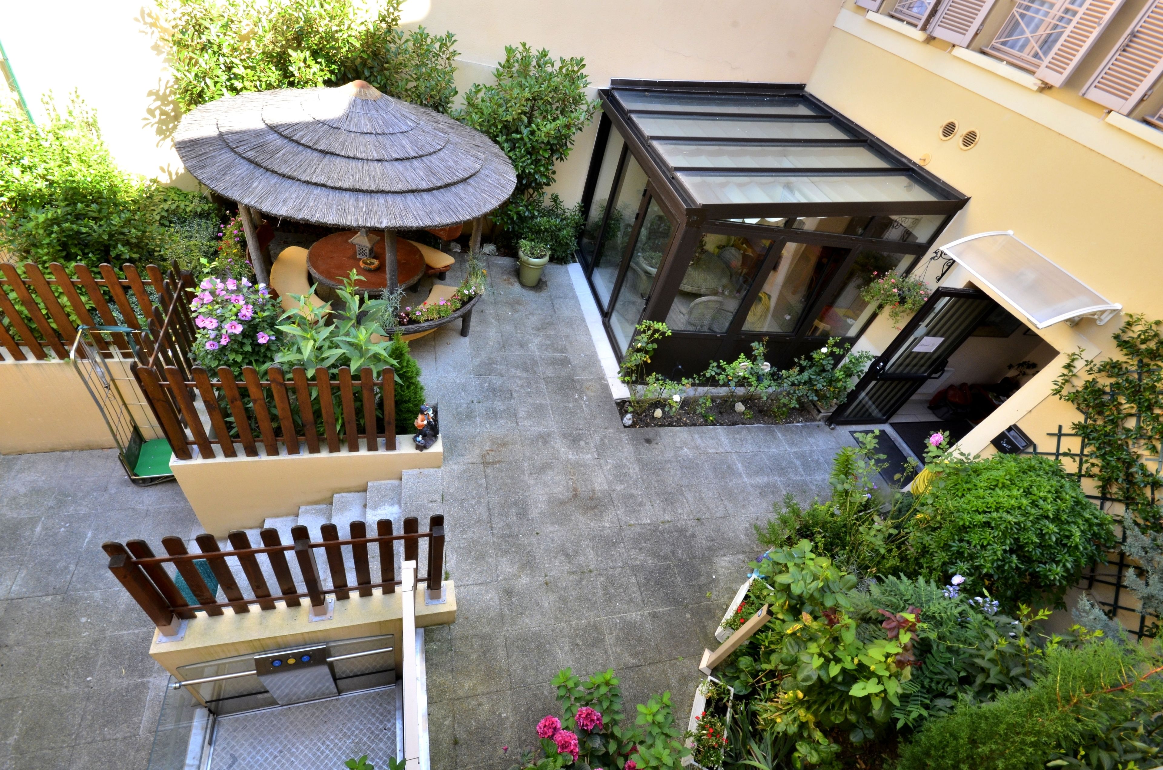 A courtyard with a thatched-roof gazebo, potted plants, and a glass-enclosed structure.