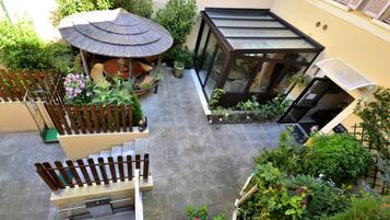 A courtyard with a thatched-roof gazebo, potted plants, and a glass-enclosed structure.