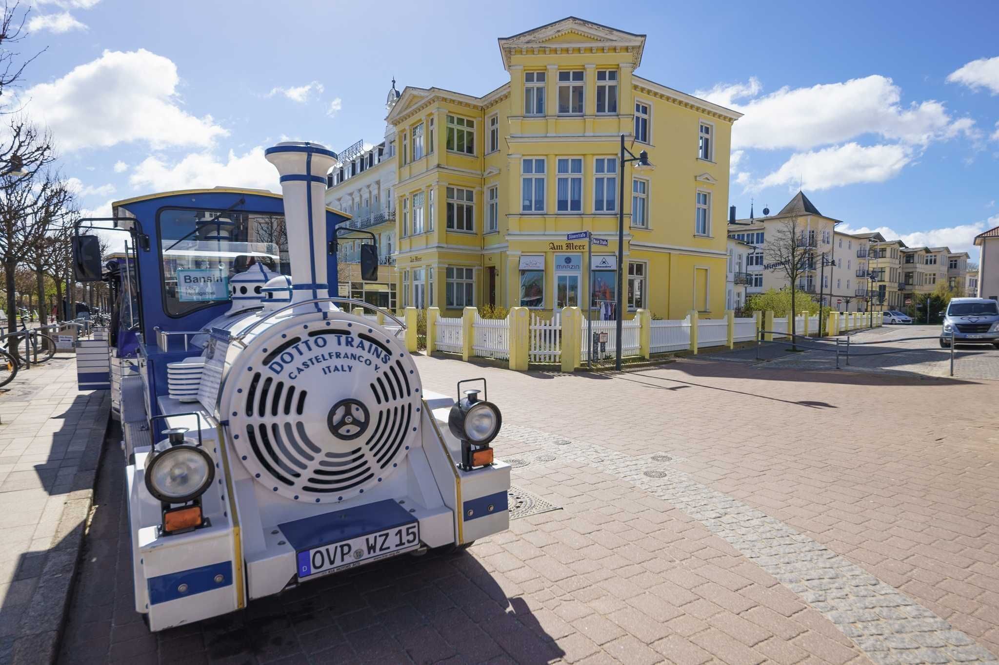 A vintage train model parked in front of a yellow building with a sign that reads 'Am Hotel.'