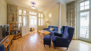 A living room with a sofa, ottoman, and a TV on a wooden table. - Vacation apartment 6 - Villa HENRIETTE (Heringsdorf)