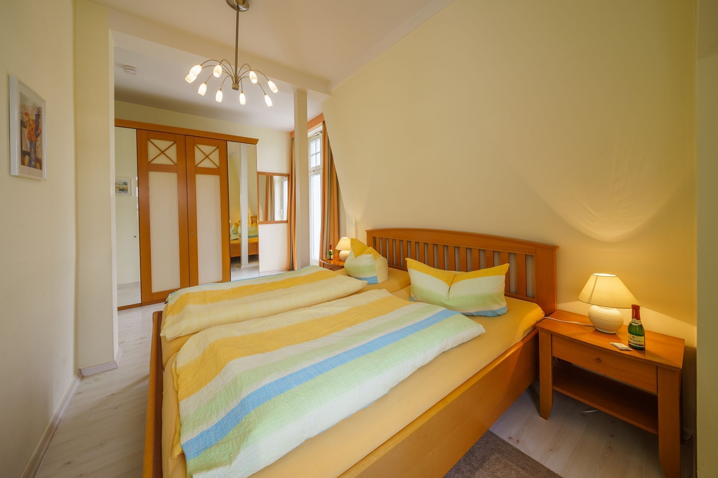 Ein Schlafzimmer mit einem großen Bett, einem Holzkopfende, Nachttischen mit Lampen und einem Spiegel.