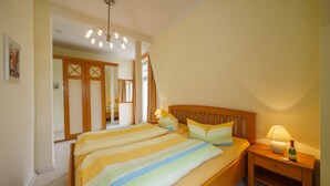 A bedroom with a large bed, wooden headboard, bedside tables with lamps, and a mirror. - Vacation apartment 6 - Villa HENRIETTE (Heringsdorf)