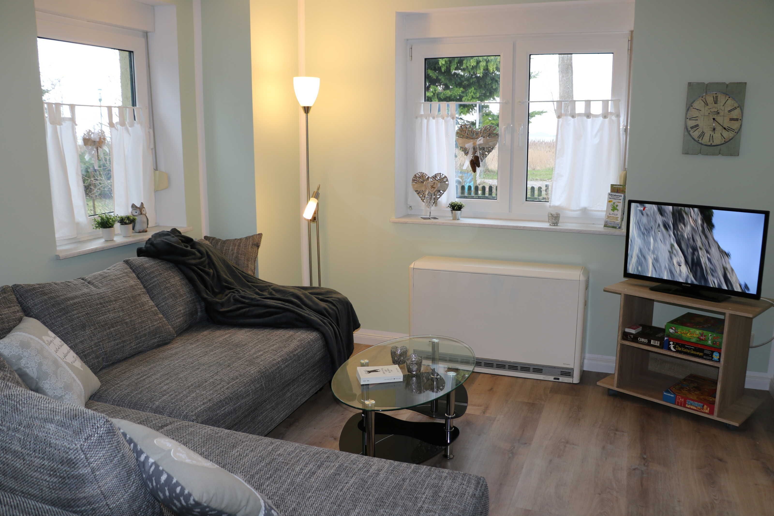 A living room with a sofa, a glass coffee table, a TV on a stand, a radiator, and a window with curtains.