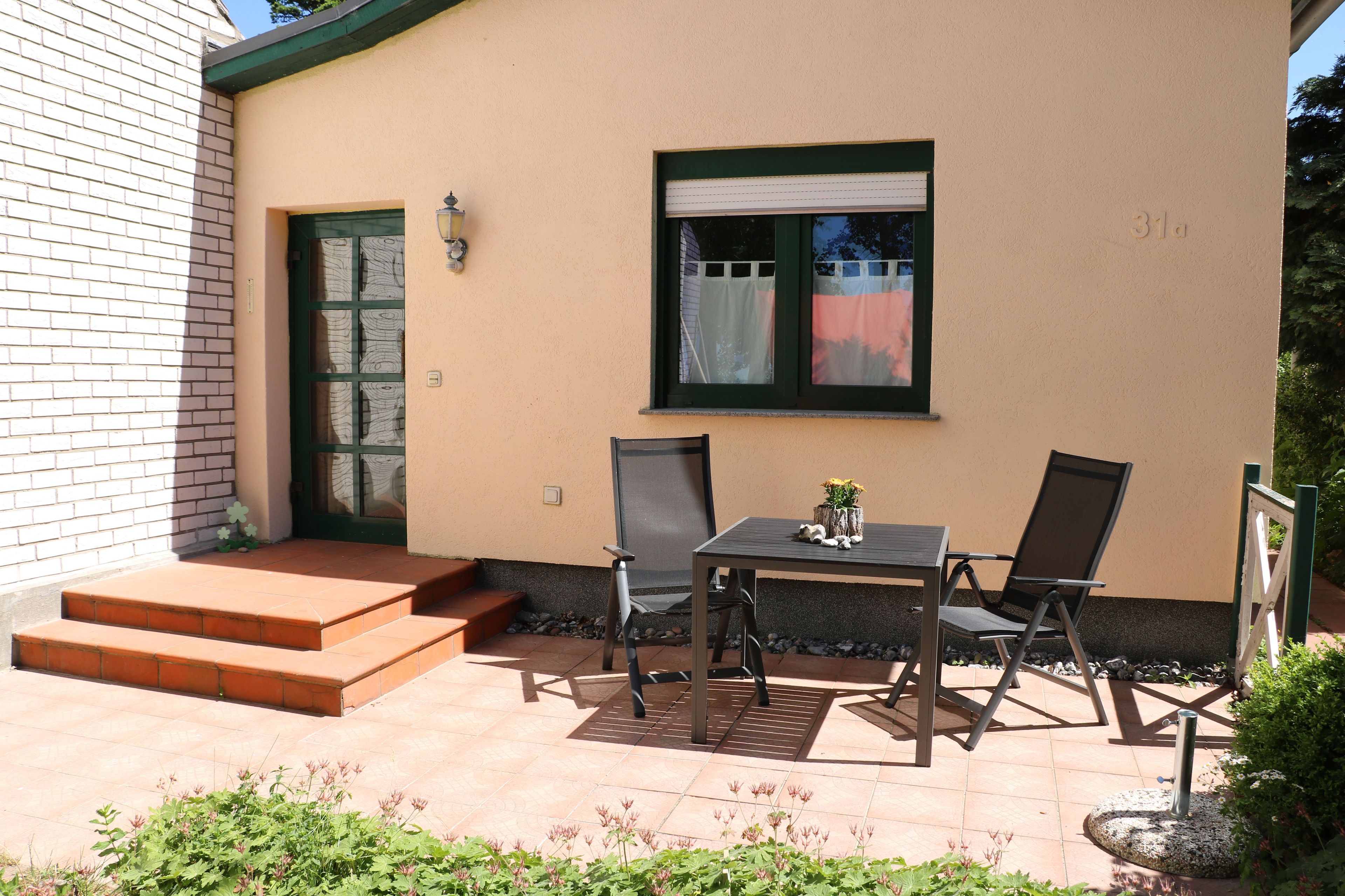A patio with a table and chairs, a door, and steps leading to a house.