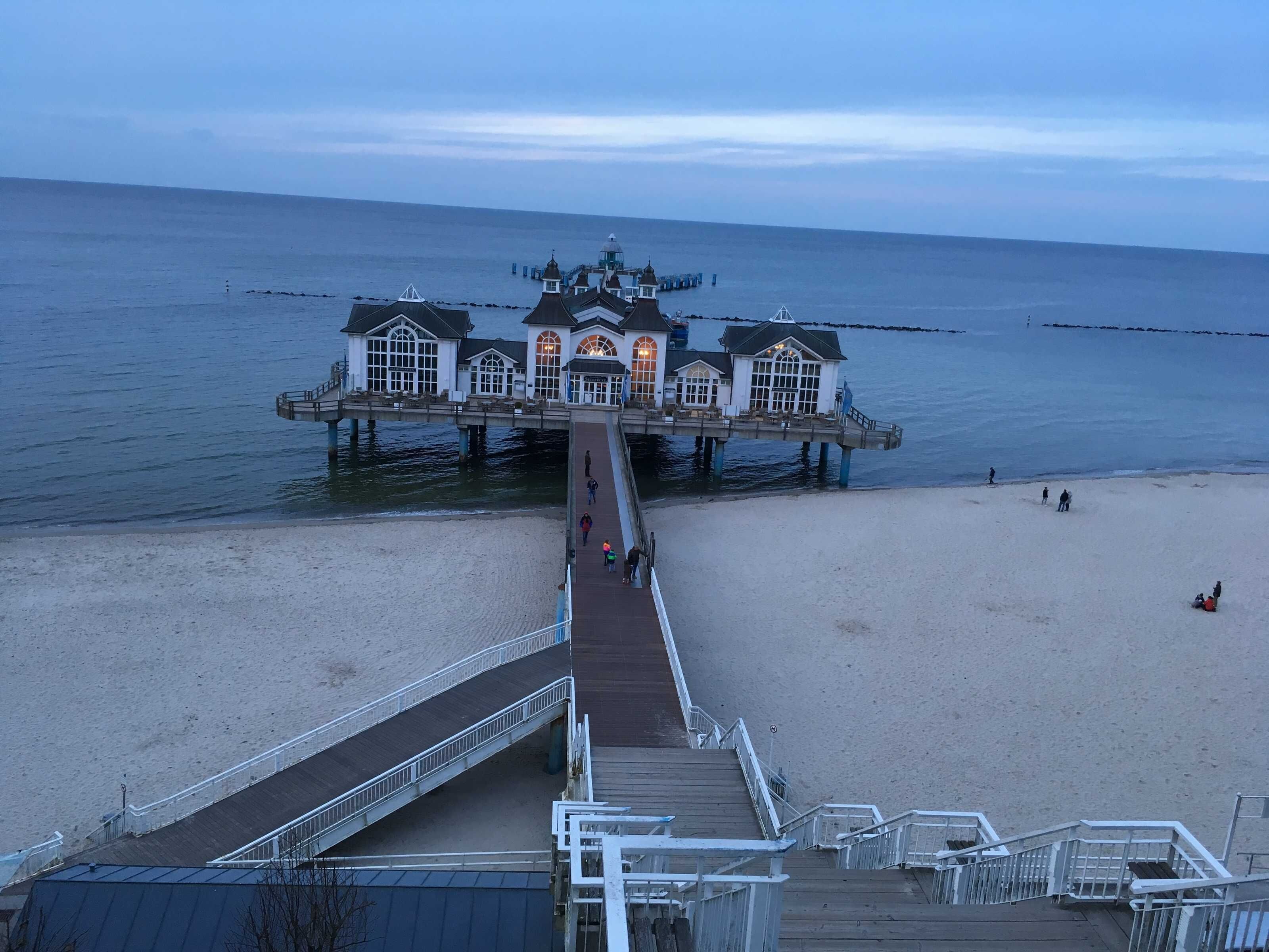A pier leading to a waterfront building with multiple windows and a dome.