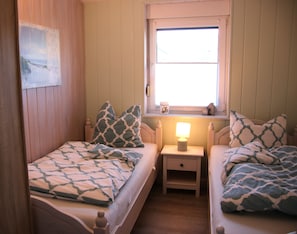 Ein Schlafzimmer mit zwei Betten, jeweils mit gemusterten Betttextilien, einem Nachttisch mit Lampe und einem Fenster mit Blick.