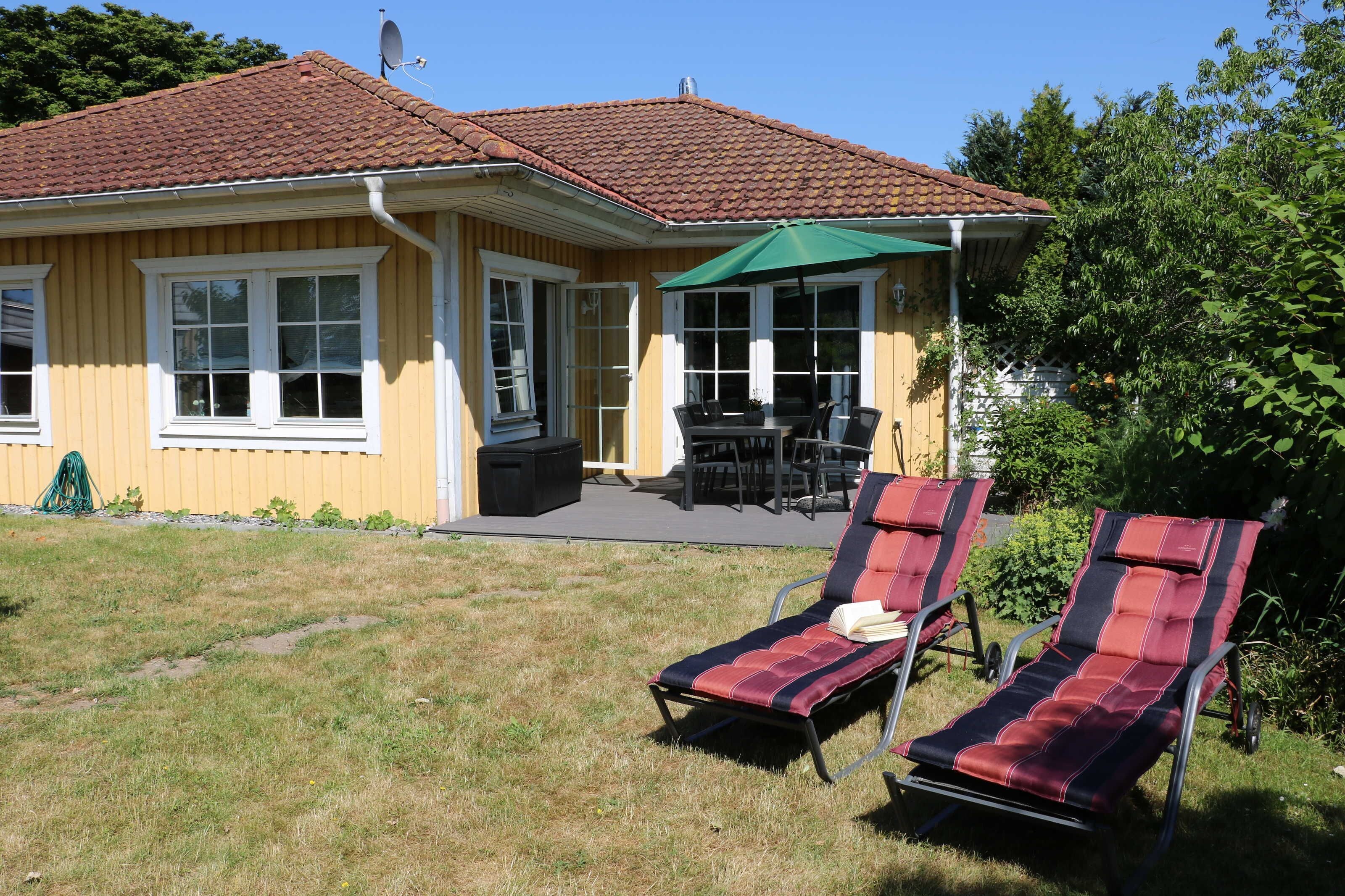 A yellow house with a red-tiled roof, a patio with a table and chairs, and two lounge chairs.