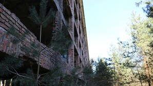 A brick building with a partially open structure, surrounded by pine trees. - Apartment Bodden - View of the water - Apartments Polchow - directly at the (Glowe)