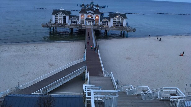 A pier leading to a waterfront building with multiple windows and a dome. - Apartment Bodden - View of the water - Apartments Polchow - directly at the (Glowe)