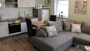 A modern kitchen with a microwave, oven, and dining area. There is a sofa with decorative pillows and a window with butterfly artwork. - Apartment Bodden - View of the water - Apartments Polchow - directly at the (Glowe)