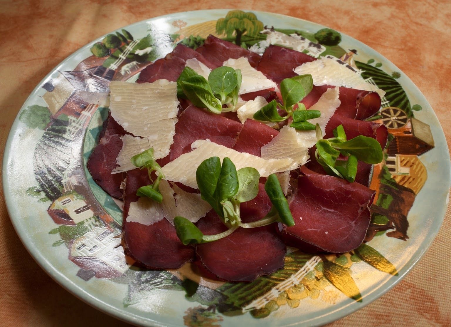 Un plato de embutidos con queso y vegetales verdes.