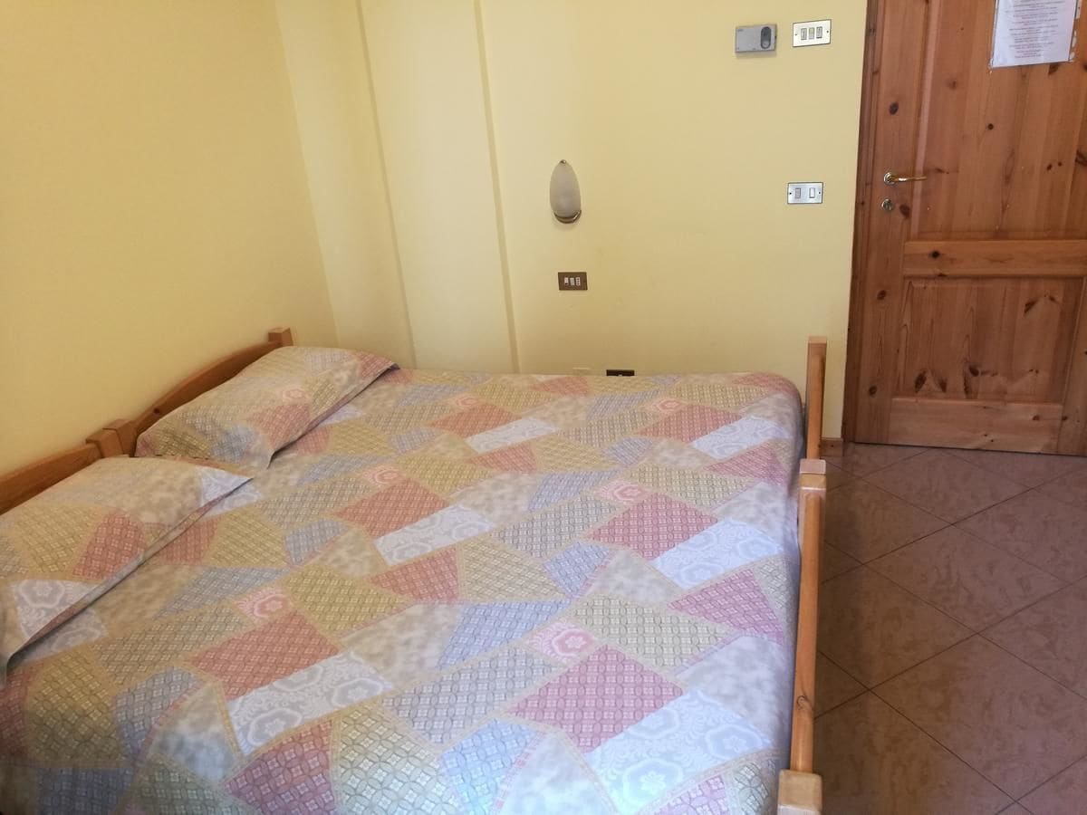 Un lit simple avec une couverture à motifs, une porte en bois et un interrupteur sur le mur.