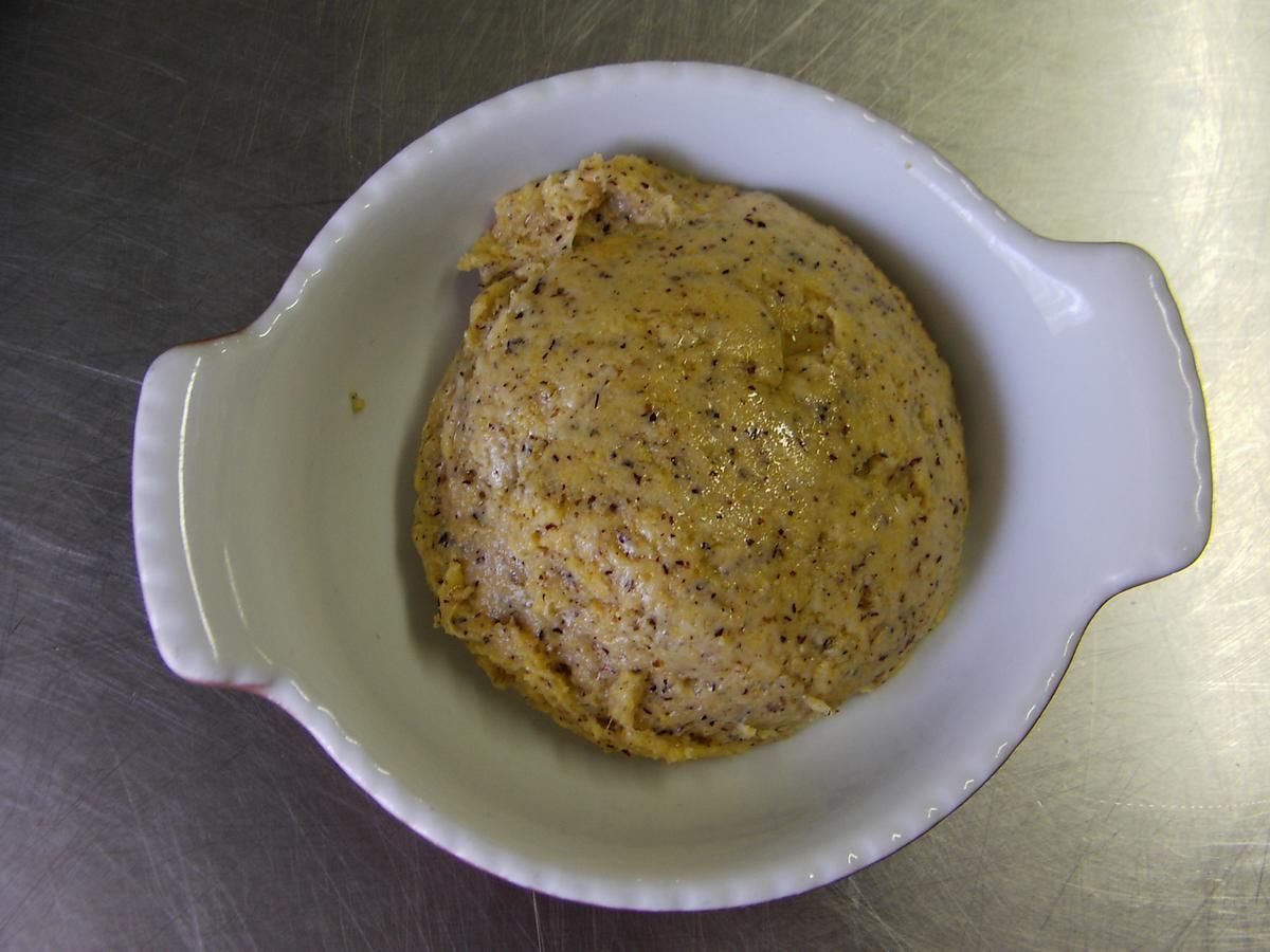 Un cuenco de cerámica blanca que contiene un alimento con motas visibles, posiblemente hierbas o especias, sobre una superficie metálica.