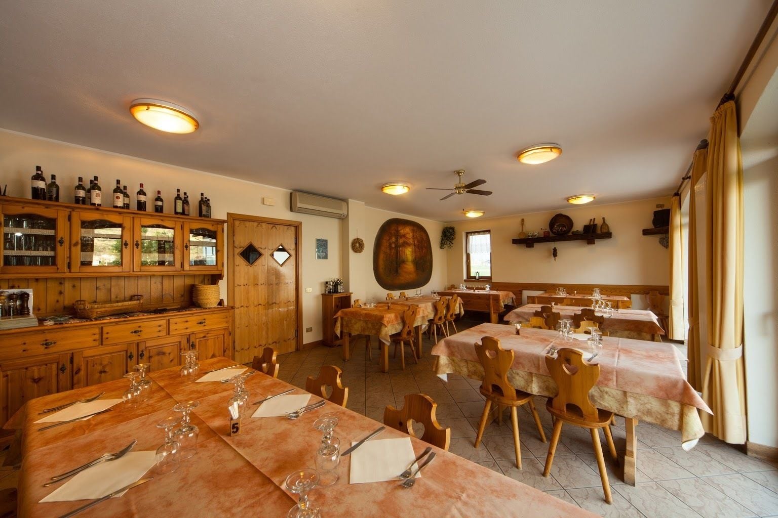 Un restaurant avec des tables et des chaises en bois, un meuble à vin et un ventilateur au plafond.