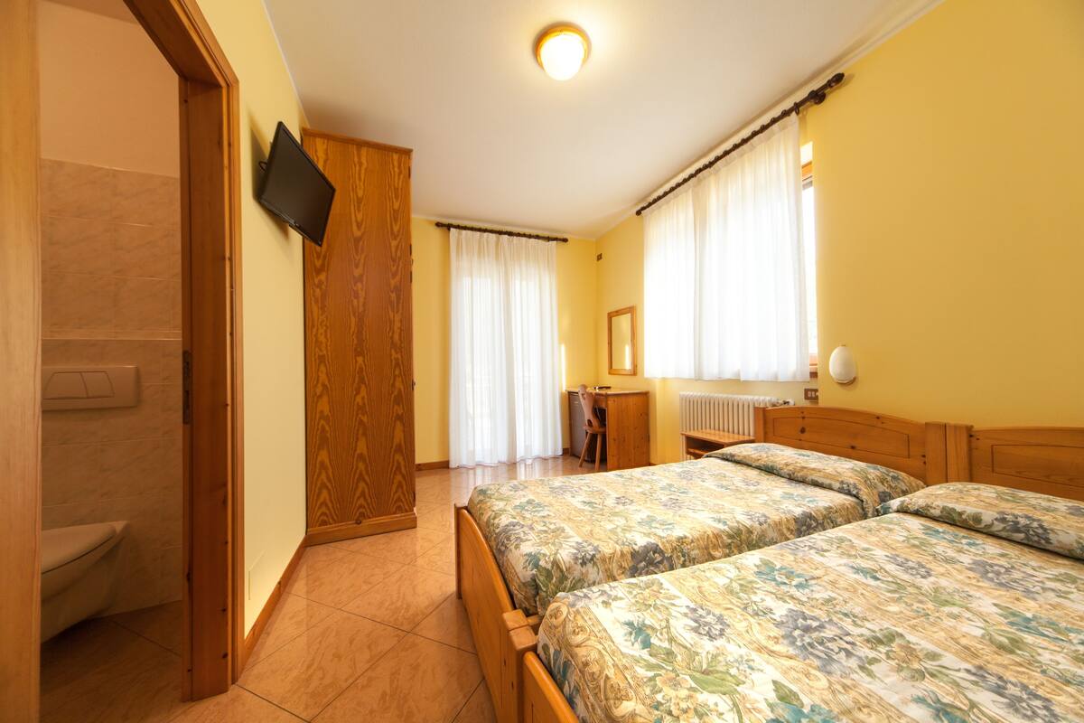 Ein Schlafzimmer mit zwei Betten, einem Holzschrank, einem Schreibtisch und einem Fernseher an der Wand.