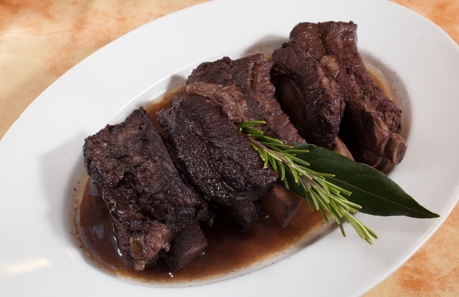Un plato de carne estofada con salsa y decoración de romero.