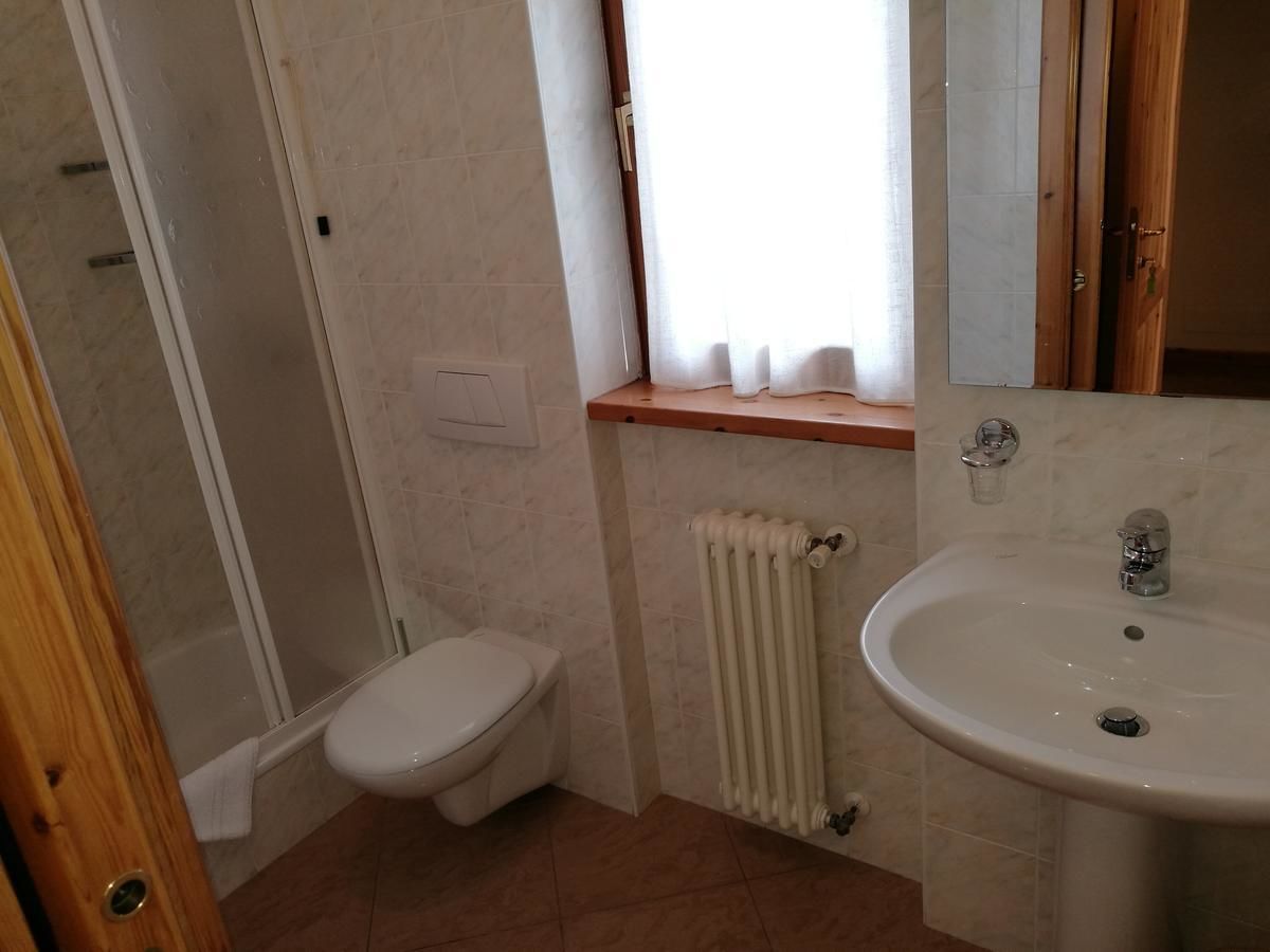 A small bathroom with a toilet, a sink, a window with curtains, and a shower area.