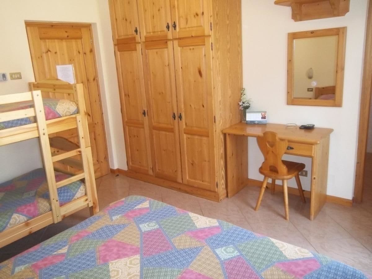 Un dormitorio con literas, un escritorio con silla, armarios de madera y un espejo.