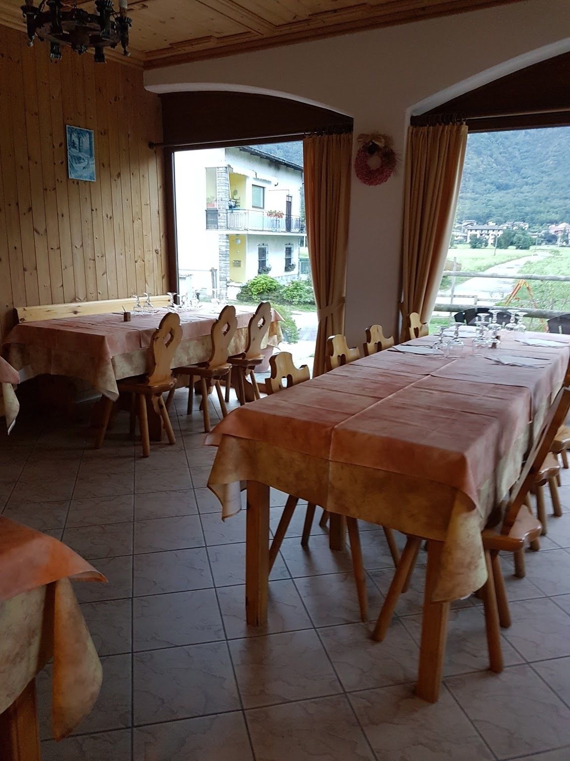 A dining area with wooden tables and chairs, a view of a building and mountains through the windows.