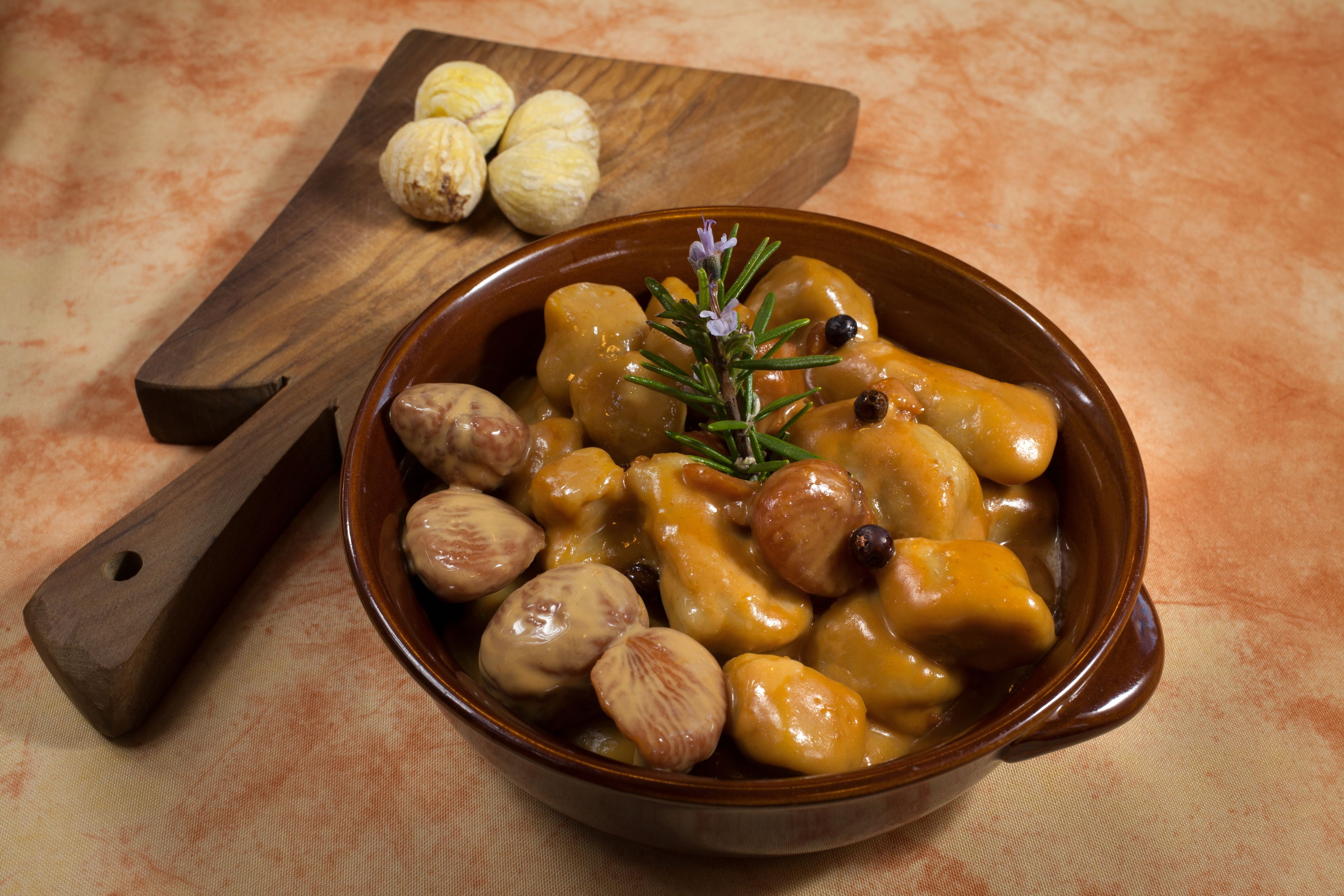 A bowl of food with nuts and a sprig of rosemary.