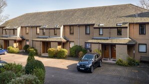 A row of townhouses with a central courtyard, each with a small garden and a car parked in front. - Springfield View (North Berwick)