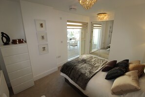 Une chambre à coucher avec un lit, une commode, un lustre et un grand miroir.