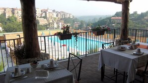A terrace with a pool, dining table, and chairs, overlooking a town and hills. - Le Rocce (Sant'Agata de'Goti)