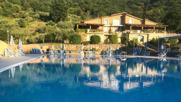 A pool with lounge chairs and umbrellas, surrounded by a hillside and a building with multiple balconies. - Le Rocce (Sant'Agata de'Goti)