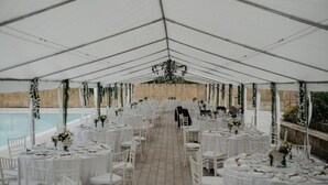 A tented outdoor event space with tables set for a formal gathering, a pool in the background, and a stone wall. - Le Rocce (Sant'Agata de'Goti)