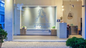 L’entrée d’un hôtel moderne, avec une façade en verre, un comptoir d’accueil et un espace détente agrémenté de plantes.
