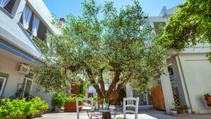 Un espace extérieur aménagé avec une table et des chaises, entouré de plantes en pot et d’un grand arbre.