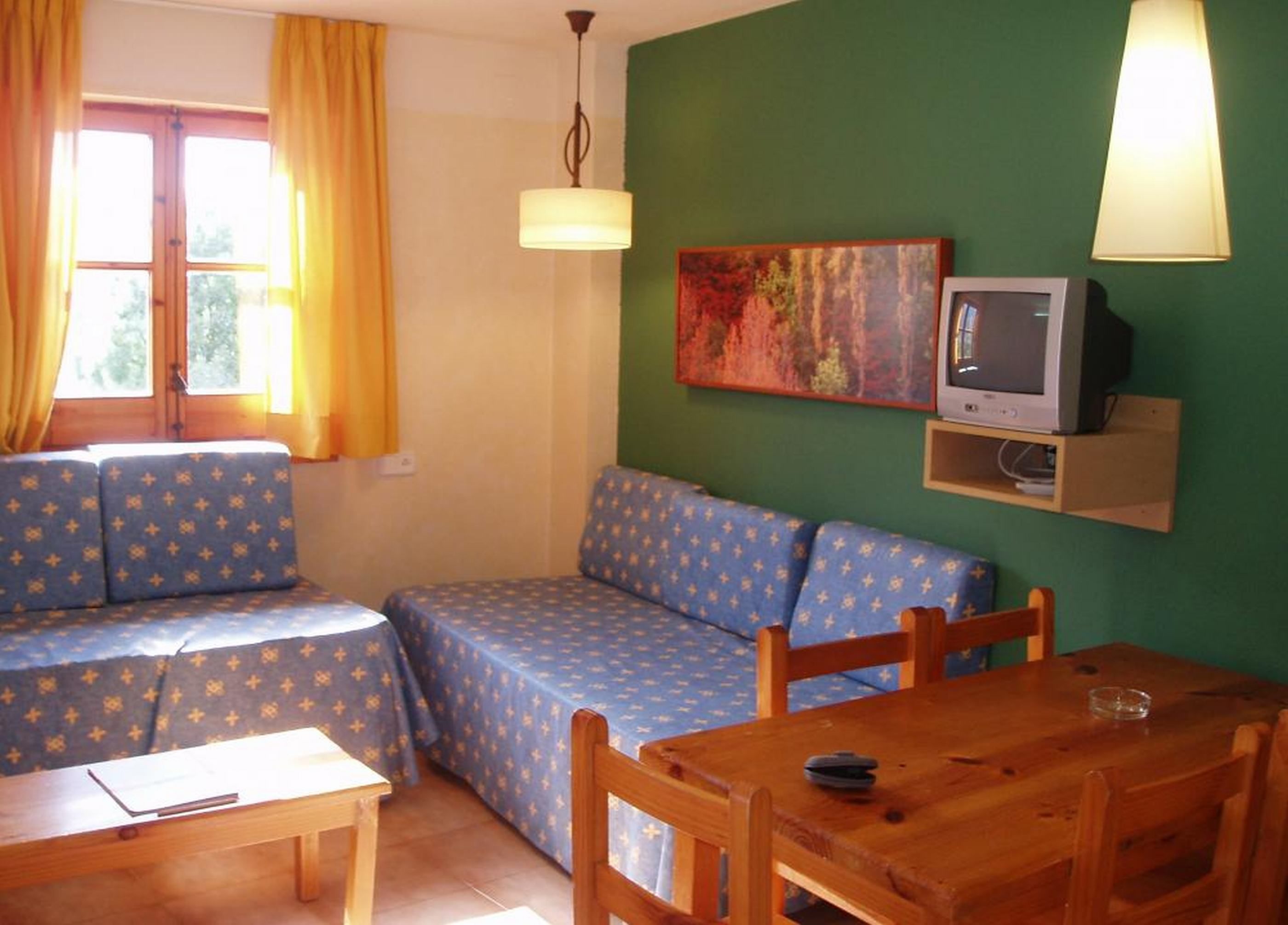 A cozy living room with a sofa set, a wooden table, and a television on a shelf.