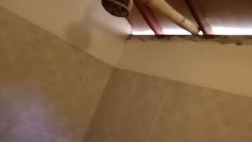 Una esquina de una habitación con suelo de baldosas, una puerta de madera y un accesorio de fontanería a la vista.