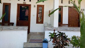 A building facade with three wooden doors, a small staircase, and a trash bin. - Sari Laut (Gili Meno)