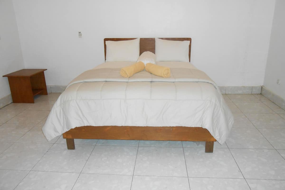 A bed with a wooden frame and white bedding, a small wooden nightstand, and a plain white wall.