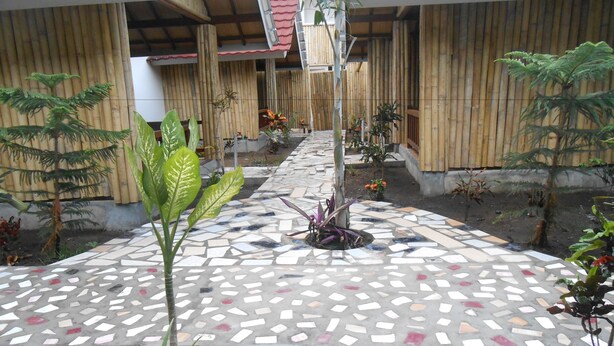 A courtyard with a mosaic-tiled walkway, bamboo walls, and various potted plants. - Sari Laut (Gili Meno)