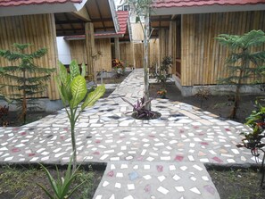 Un patio con un sendero de mosaicos, paredes de bambú y diversas plantas en macetas.
