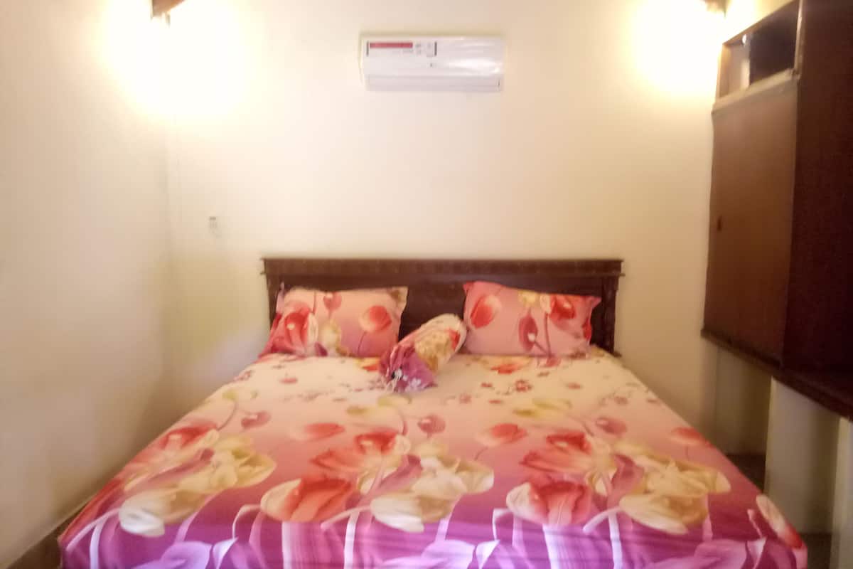 A bed with floral bedding, a wooden headboard, and a wall-mounted air conditioning unit.